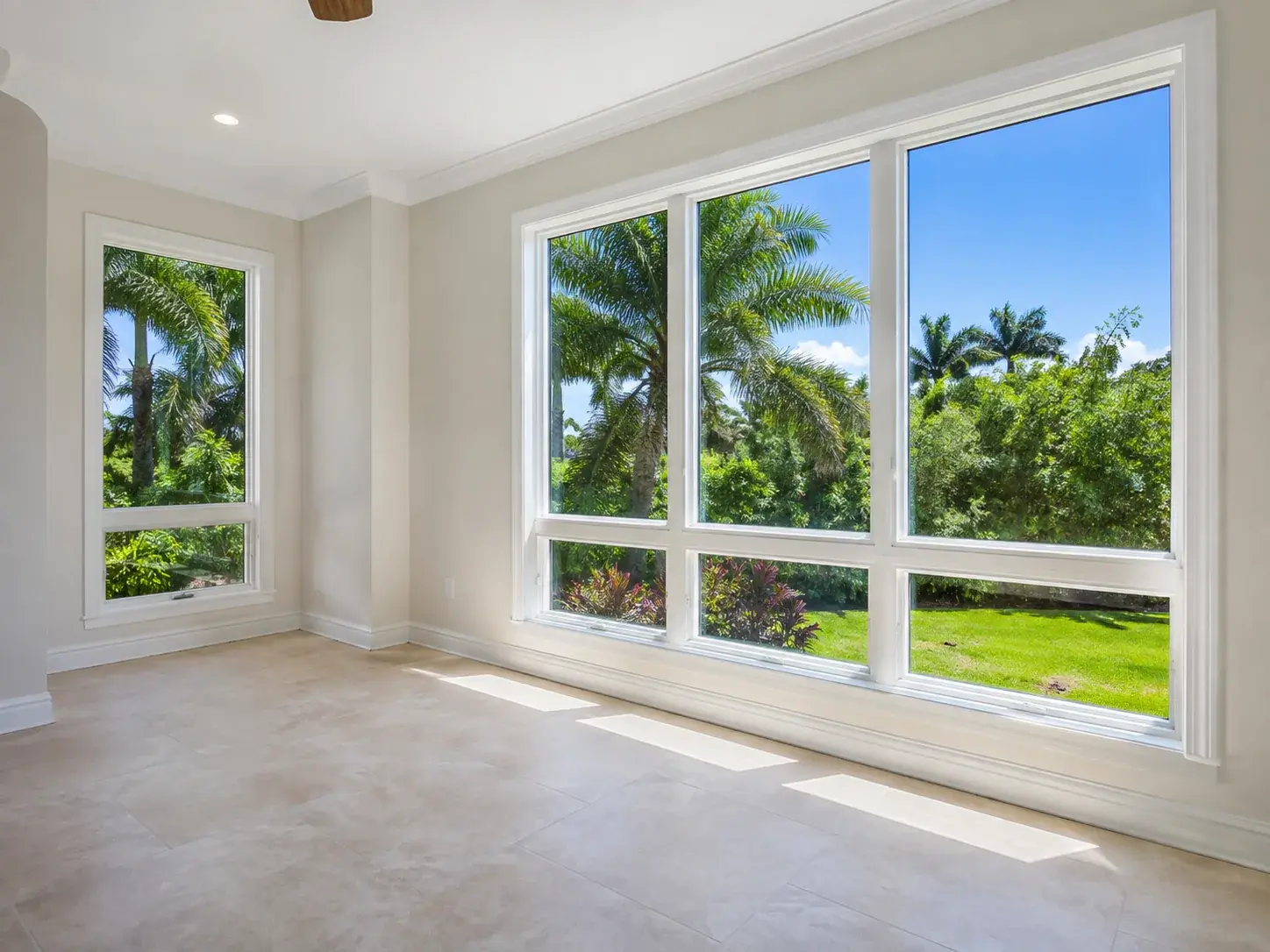 Interior view of large white-framed impact-resistant window units in a Florida home, looking out onto palms and lawn